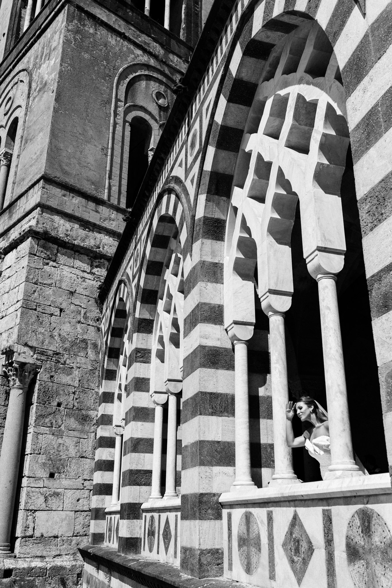 Bride peering out between the striped arches and slender columns of the cathedral's arcaded facade