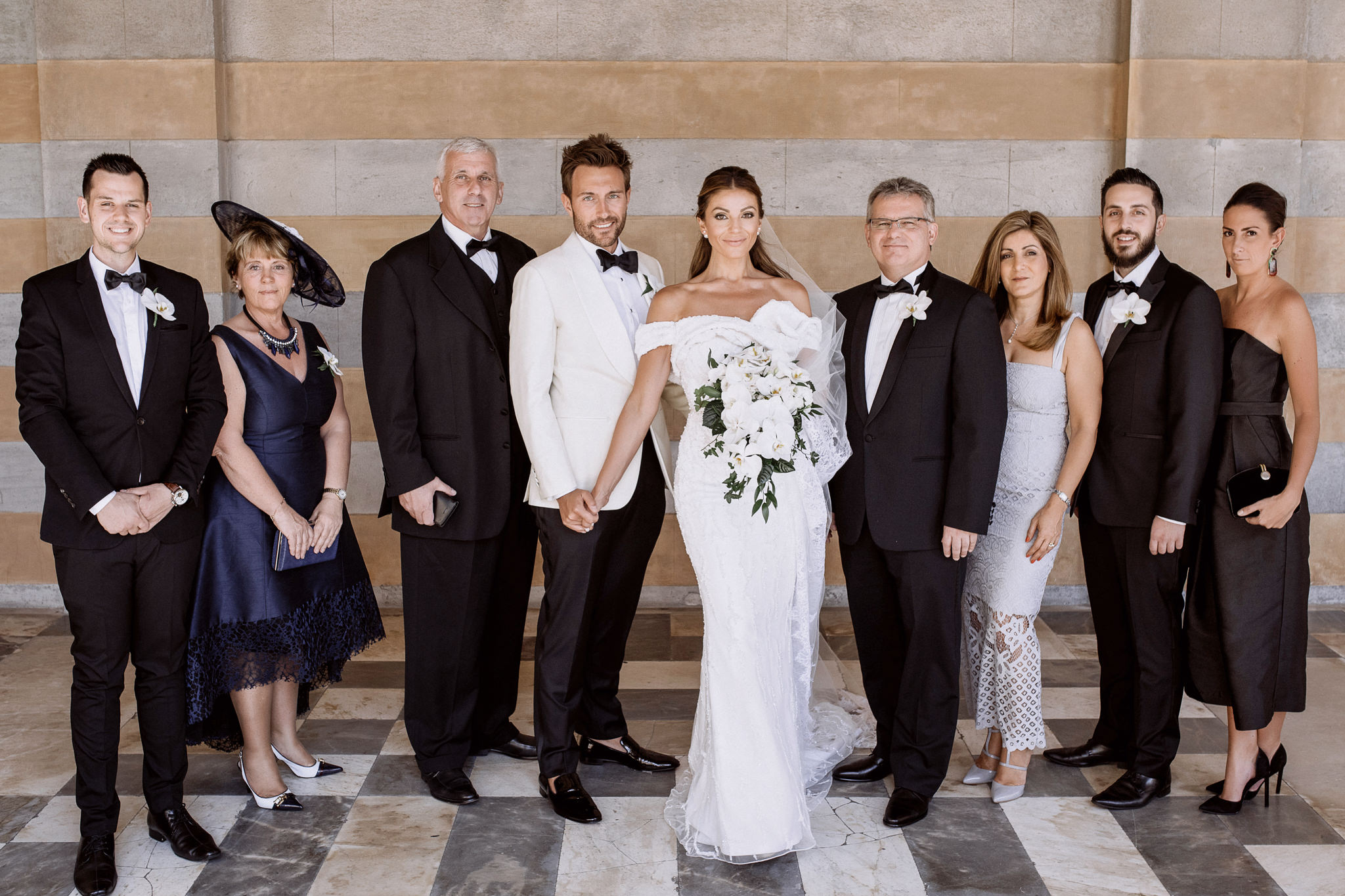 Portrait of the bride and groom with guests in black tie under a striped stone portico