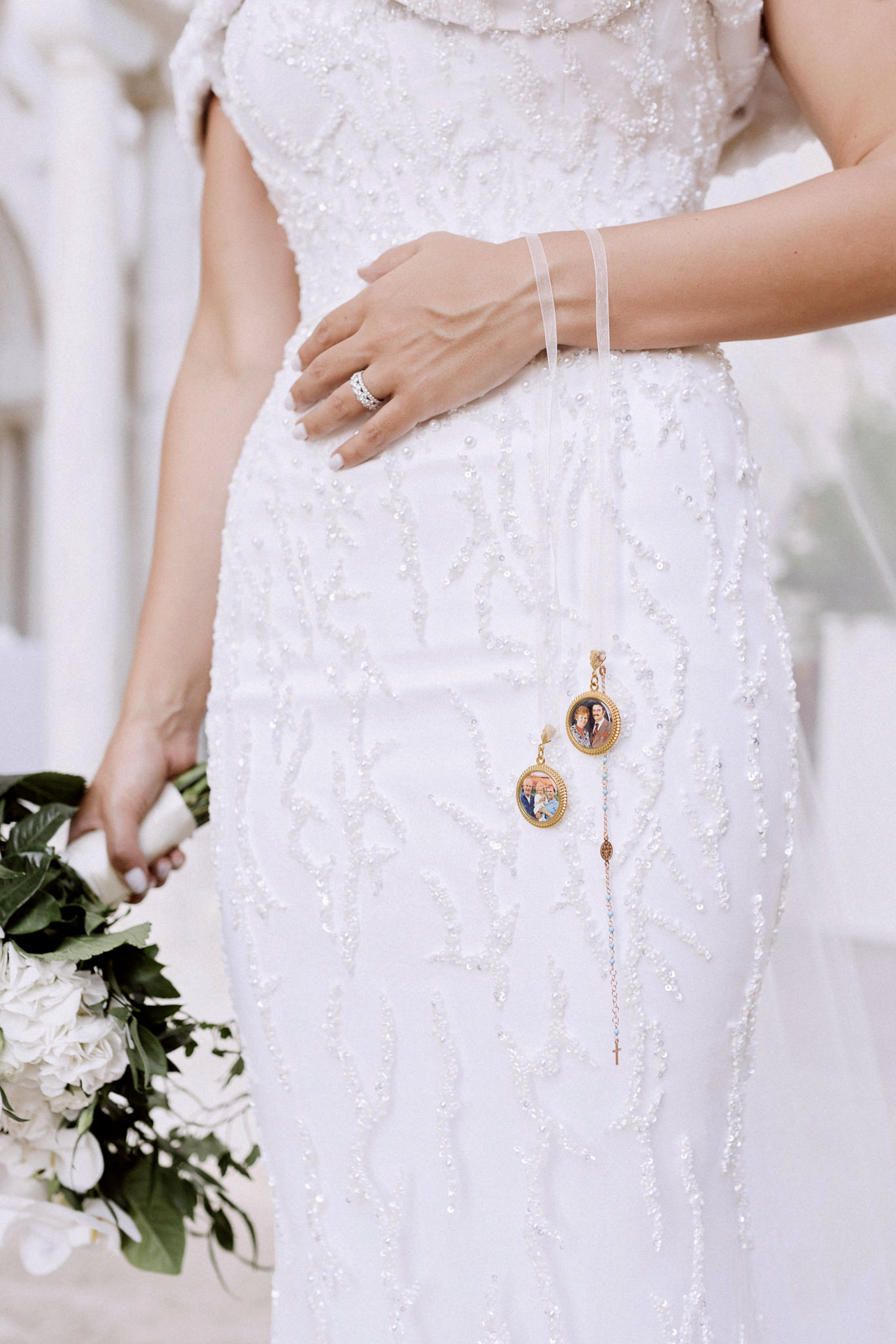 Gold photo memorial charms on ribbons hanging from the bride's wrist against her beaded gown