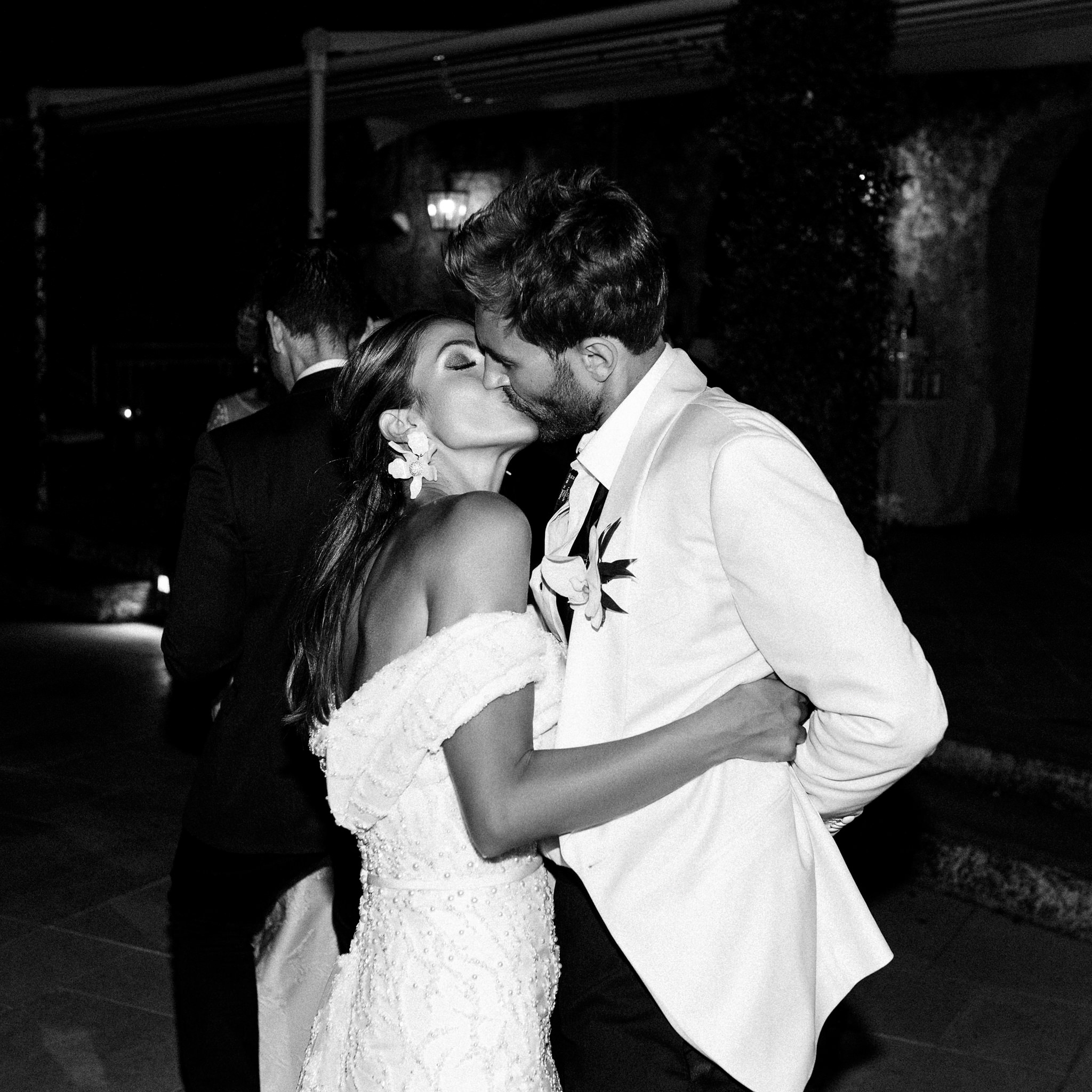 Bride with an orchid earring kissing the groom on the dance floor at night